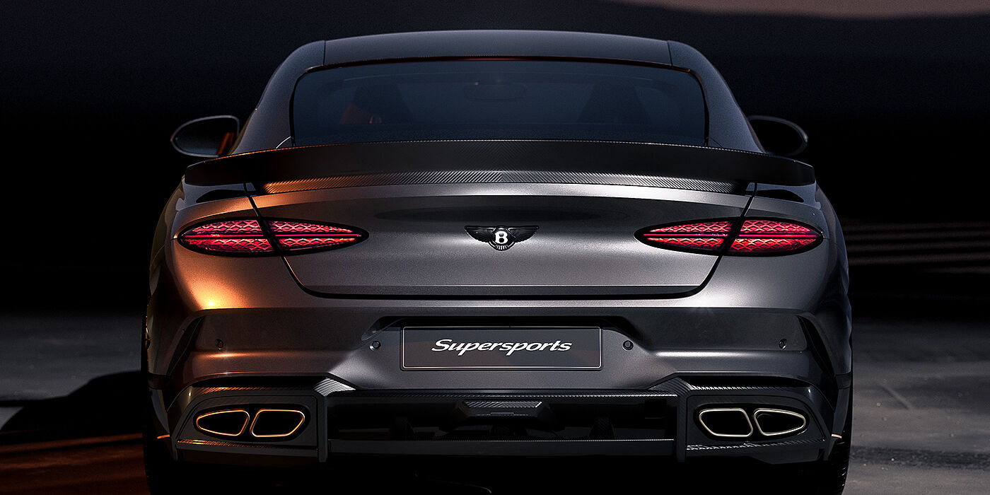 Gohm Sportwagen GmbH | Bentley Stuttgart Bentley Supersports rear view with illuminated rear lamps, spoiler and black Bentley badge in Anthracite paint against a dark grey and red background