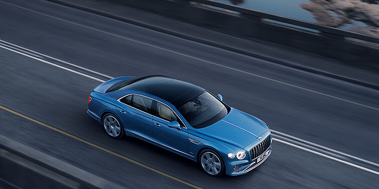 Gohm Sportwagen GmbH | Bentley Stuttgart New Bentley Flying Spur Azure sedan in Light windsor blue paint by Mulliner, with 22 inch Azure wheels seen from overhead driving dynamically on a country road